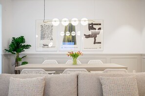 A modern dining area with a white table, white chairs, and a vase of tulips. There are framed artworks on the wall and a potted plant to the left. - "La Bella Easo" new, ac, design, near La Concha (Donostia-San Sebastian)