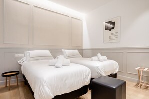 A hotel room with two beds, a small round table, a bench, and a framed picture on the wall. - "La Bella Easo" new, ac, design, near La Concha (Donostia-San Sebastian)