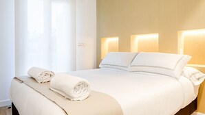 A neatly made bed with white linens and a rolled towel, a bedside table with a lamp, and a window with curtains. - "The Palms" new, ac, terrace, calm near Old Town (Donostia-San Sebastian)