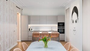 Una cocina moderna con armarios blancos, una isla central y un comedor con mesa de mármol y sillas de mimbre.