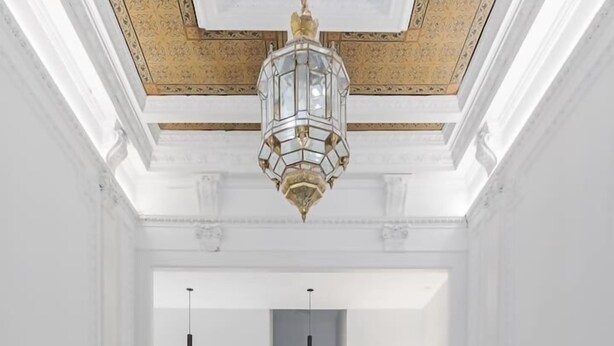 Un pasillo espacioso con piso de mármol, techo decorativo y una consola de madera oscura con jarrones.