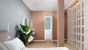 Un dormitorio moderno con cama, una planta en la mesita de noche, un tocador con espejo y un vestidor.