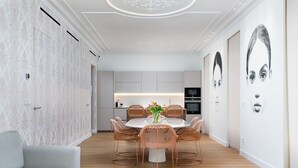 Una cocina moderna con una isla central, armarios blancos y una zona de comedor con sillas de mimbre y una mesa blanca.