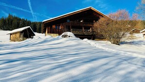 Una cabaña de madera con balcón, rodeada de nieve y árboles.