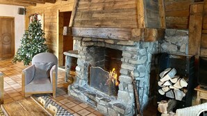 Interior acogedor de una cabaña de madera con chimenea de piedra, un árbol de Navidad y un sillón cómodo.