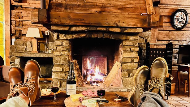 Una habitación acogedora con chimenea de piedra, una mesa de madera con comida y bebidas, y un televisor sobre un mueble de madera.