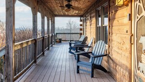 A wooden deck with Adirondack chairs, a ceiling fan, and a wooden door with a decorative handle.