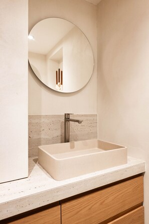 Une salle de bain avec un lavabo rectangulaire, un miroir rond et un robinet.