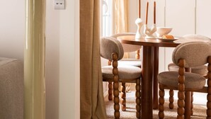 Uma sala de jantar com uma mesa redonda, quatro cadeiras, um abajur e uma porta com cortinas.