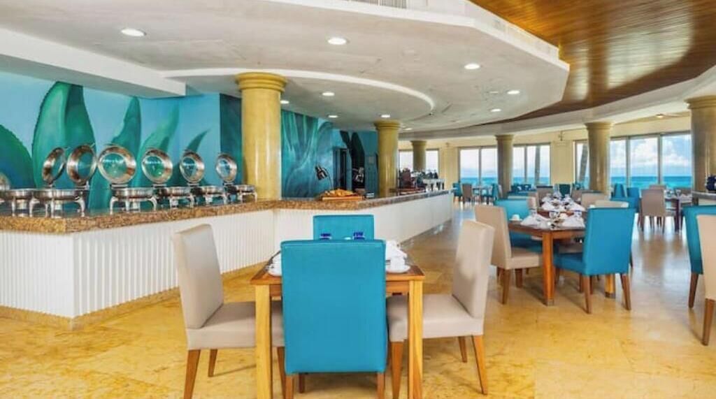 A spacious restaurant with a long counter, blue chairs, and a view of the ocean.