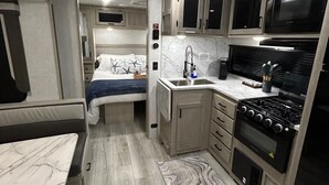 Een compact interieur van een camper met een kitchenette, een bed en een klein eethoekje.