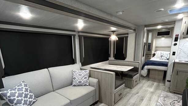 Een compact interieur van een camper, met een bank, een eettafeltje en een bed.