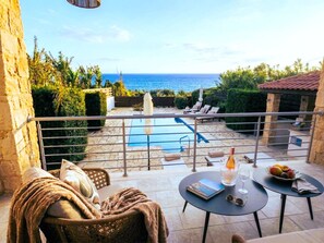 A balcony with a view of the sea, a pool, and outdoor furniture. - Beachfront Luxury Paphos Villa: 4BR, Private Pool, Hot Tub (Kissonerga)