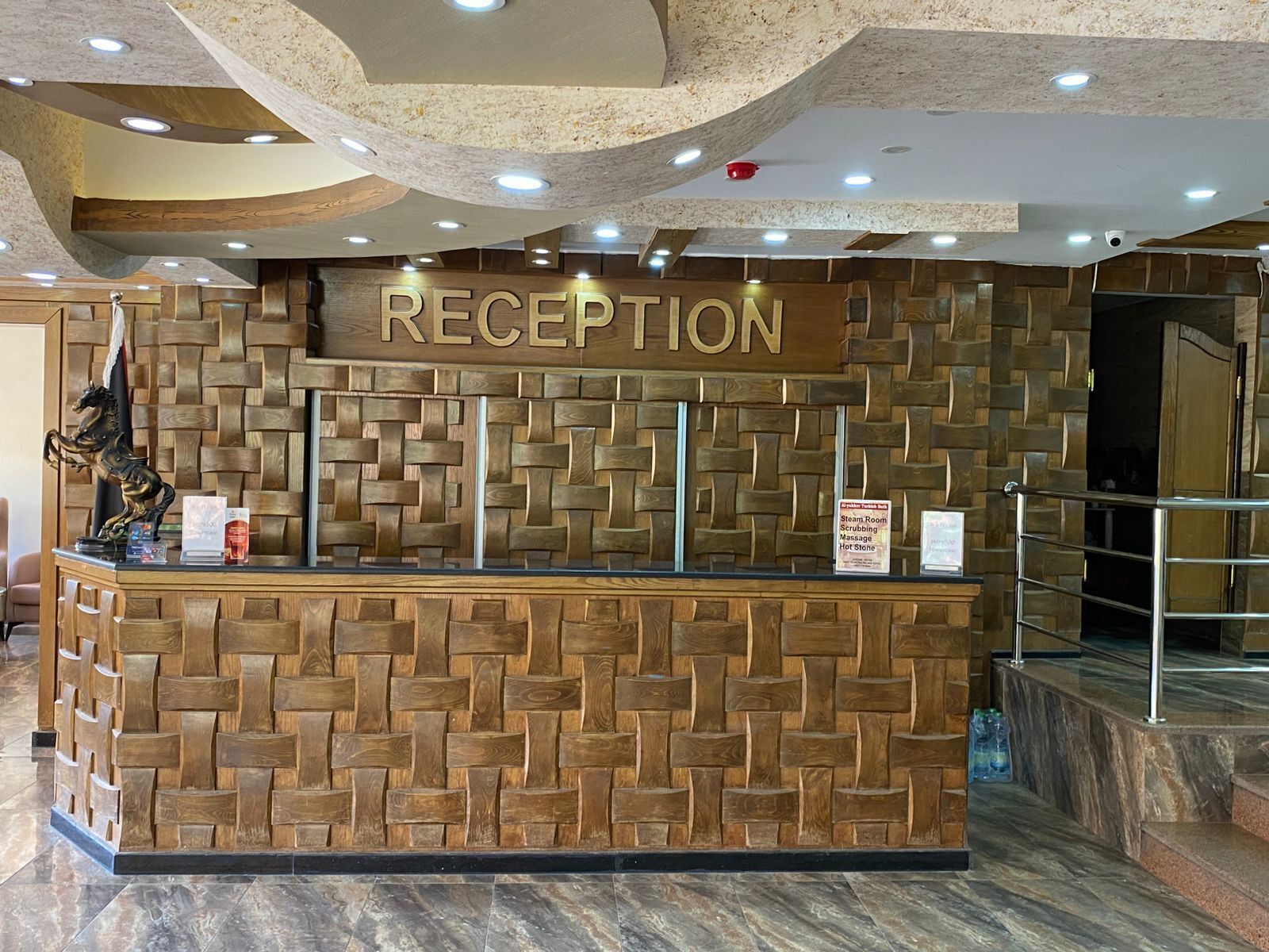 A reception desk with a wooden wall design, a sign above it, and a metal railing in the background.
