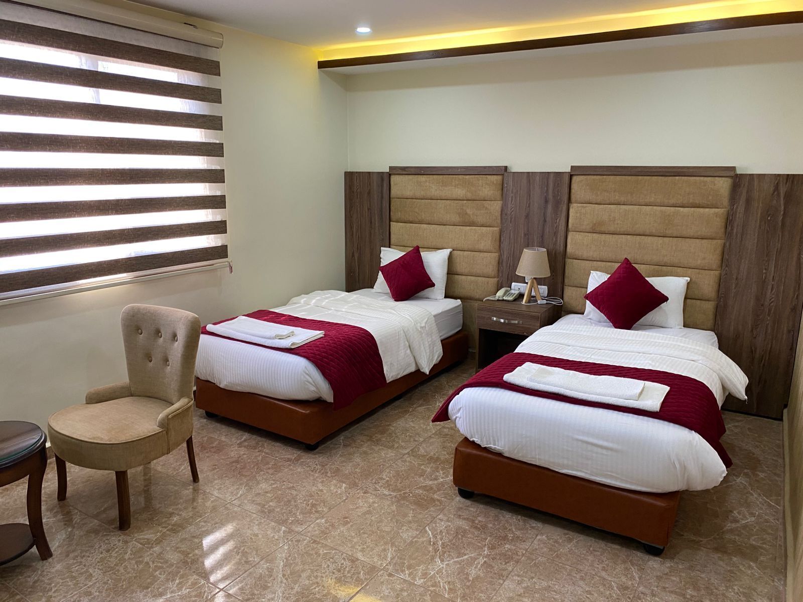 Una habitación de hotel con dos camas, una silla y una mesita de noche con lámpara.