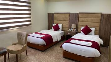 Una habitación de hotel con dos camas, una silla y una mesita de noche con lámpara.