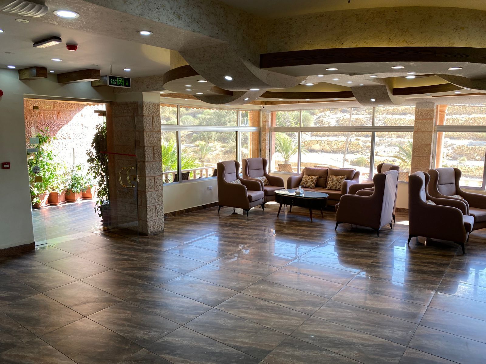 A spacious lobby with a modern design, featuring a seating area with sofas and armchairs, a central coffee table, and large windows offering a view of the outdoors.