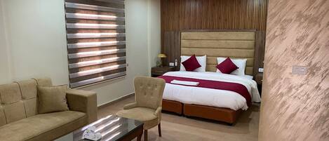 A modern hotel room with a wooden ceiling, a large bed with red and white bedding, a beige sofa, a glass coffee table, and a wooden nightstand.
