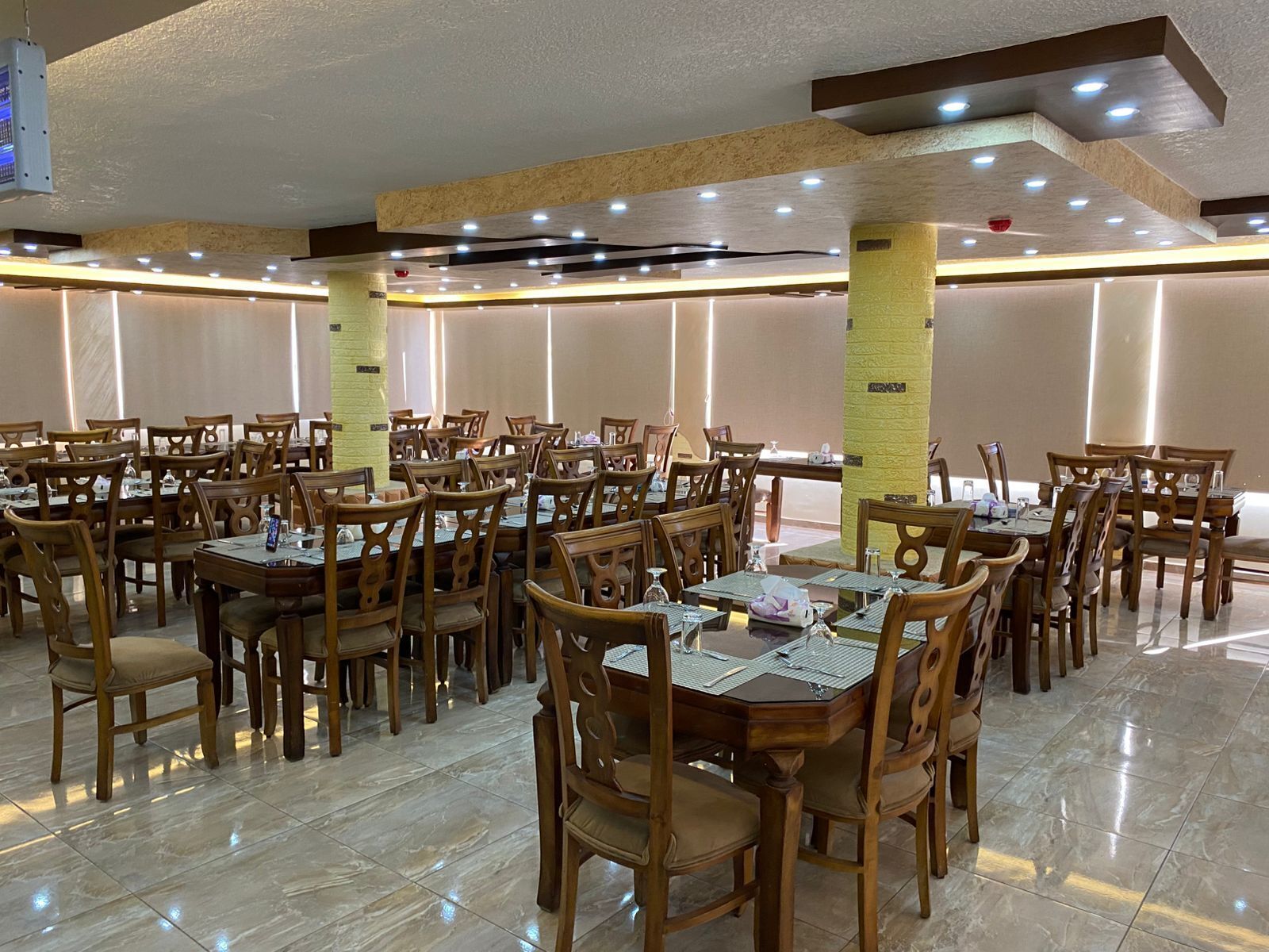 Un vaste espace dédié à la salle à manger, doté de nombreuses tables et chaises, et caractérisé par un design moderne au niveau du plafond, avec des luminaires encastrés et des colonnes décoratives.