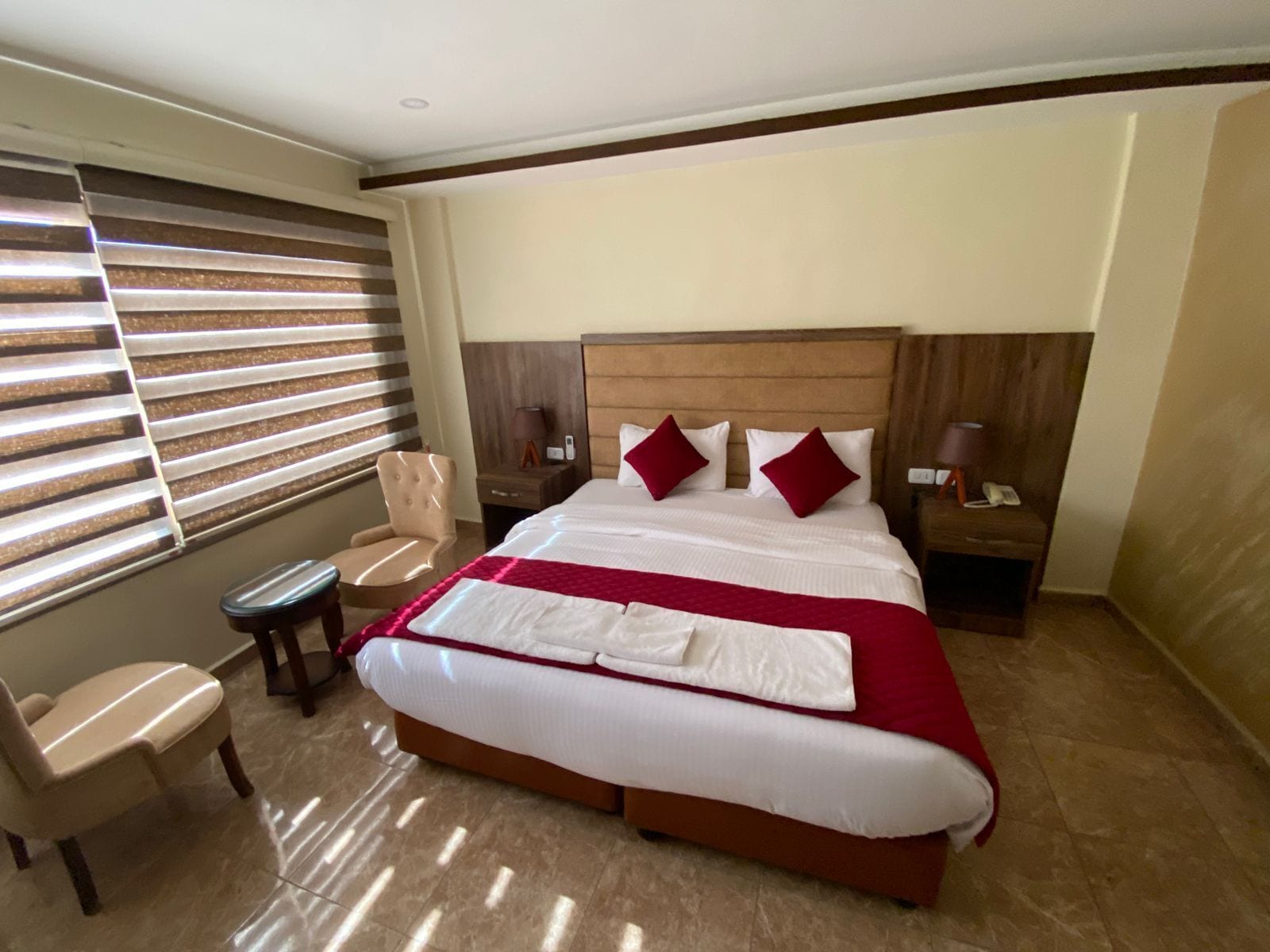 A hotel room with a large bed, a chair, a nightstand, and a lamp.