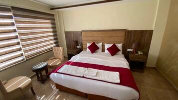 A hotel room with a large bed, a chair, a nightstand, and a lamp.