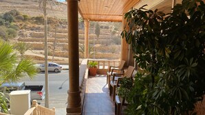 A covered outdoor area with a wooden ceiling, a balcony with chairs, and potted plants. - Sunset hotel (Wadi Musa)