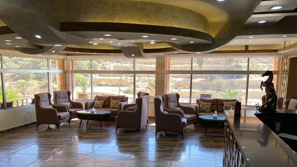 A spacious lobby with leather armchairs, a coffee table, and a reception desk. Large windows offer a view of the outdoors. - Sunset hotel (Wadi Musa)