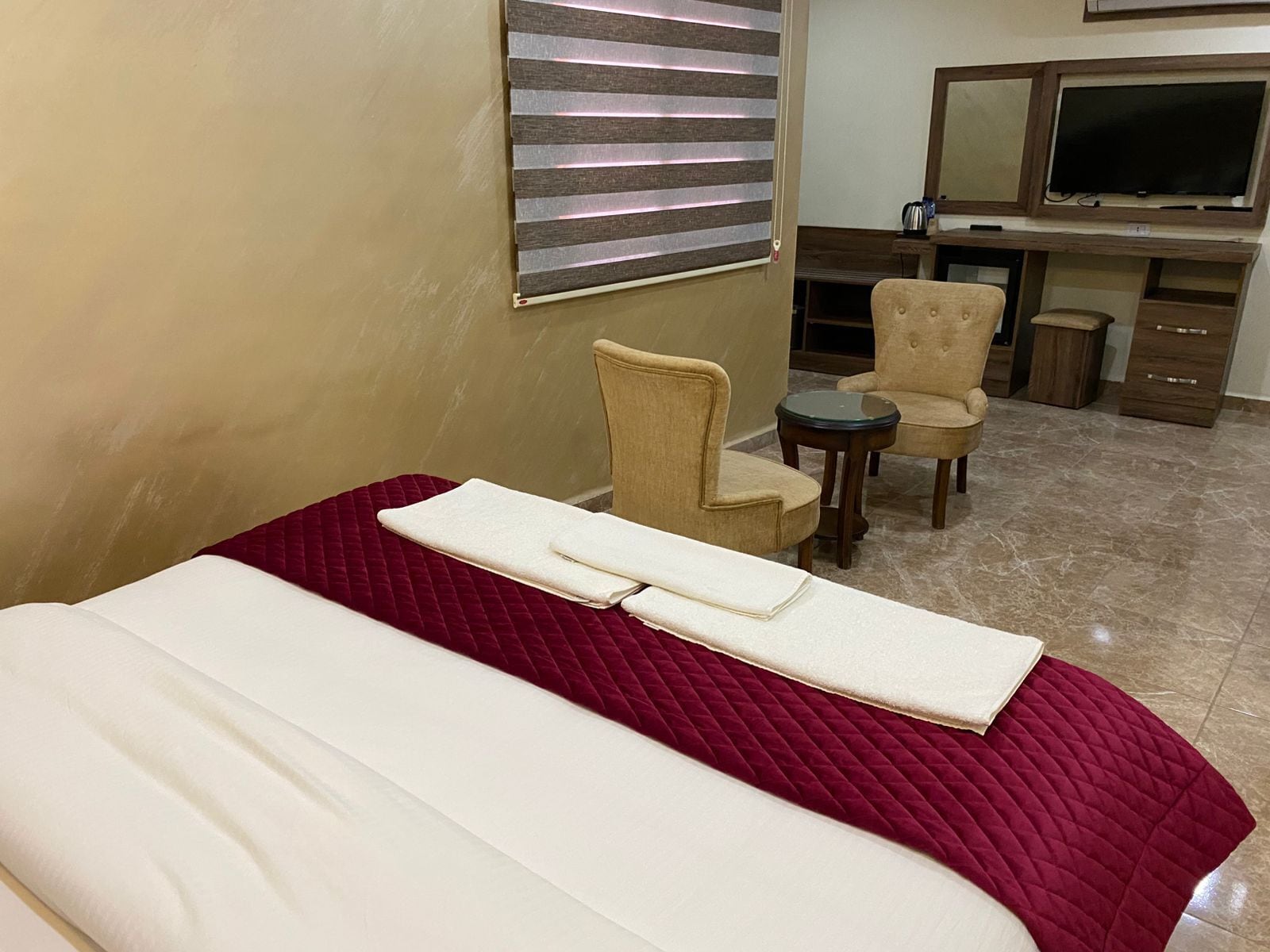 A hotel room with a bed, two chairs, a small table, a TV, and a minibar.