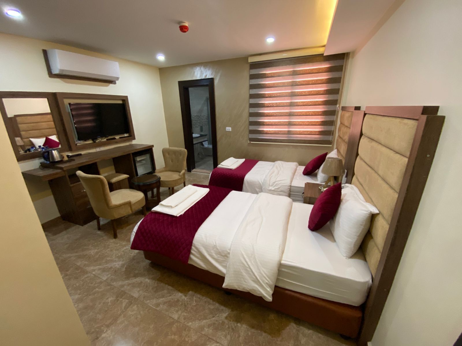 A hotel room with two beds, a desk with a TV, a chair, and a bathroom visible through the door.
