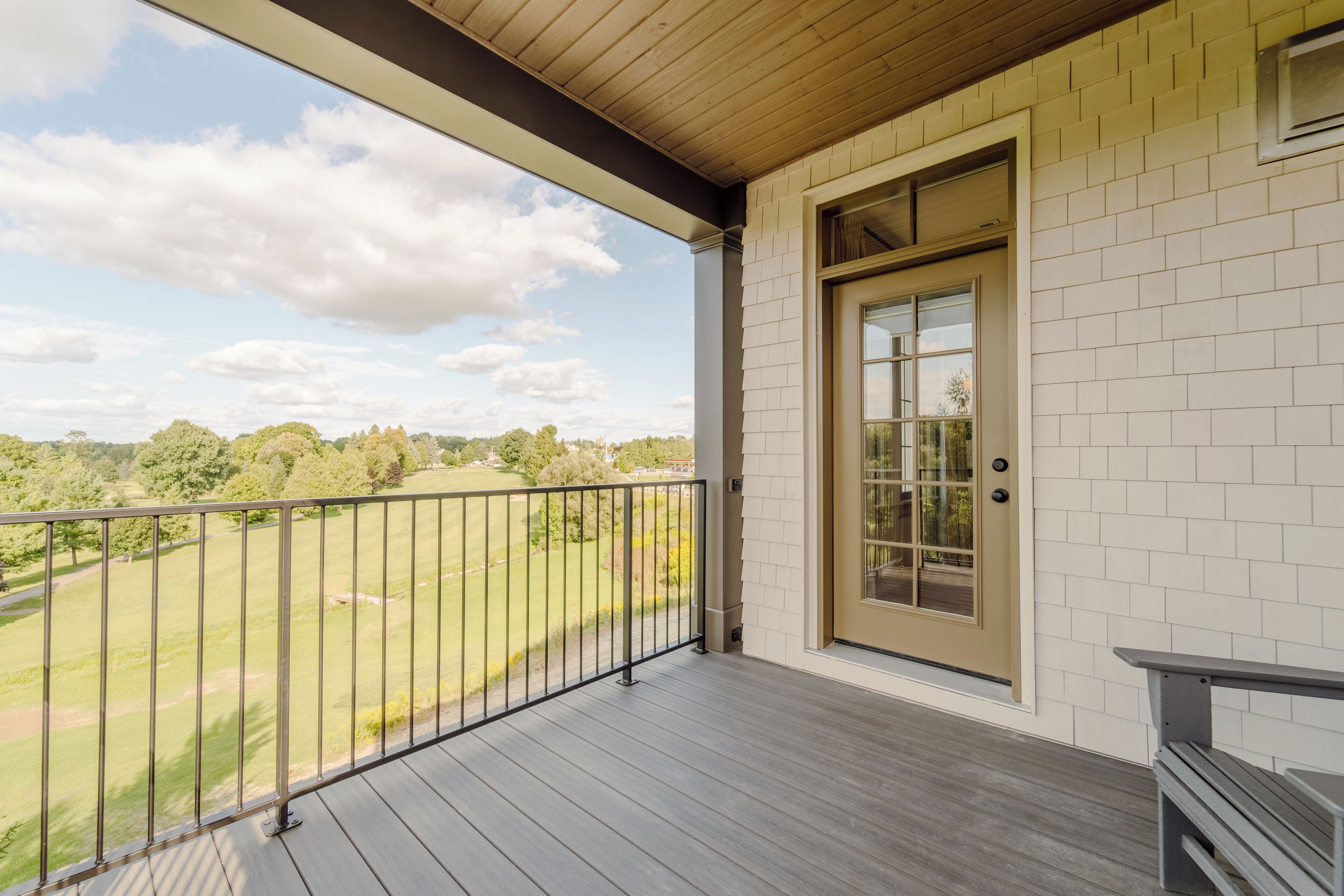 A balcony with a wooden floor and a metal railing, overlooking a green landscape.