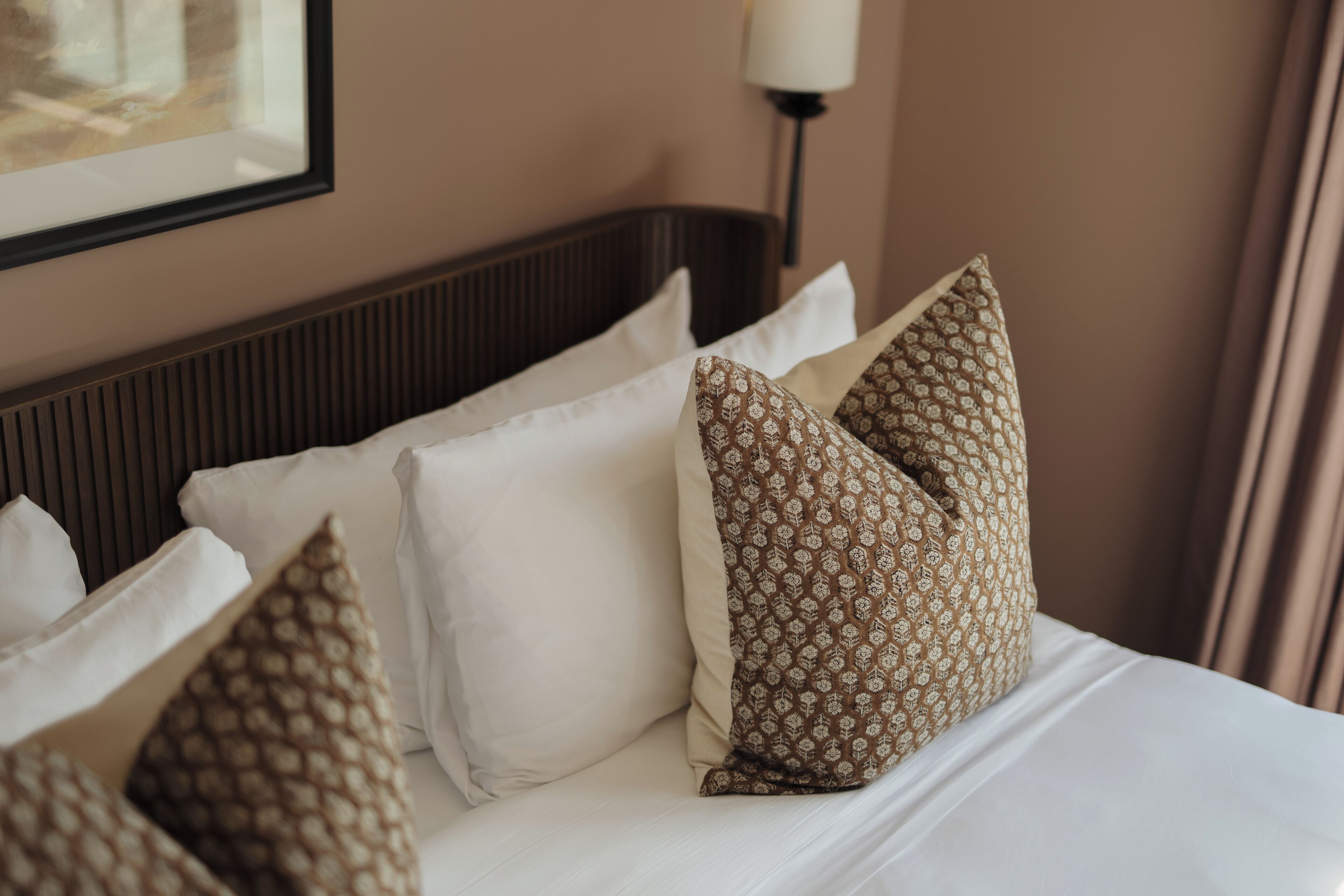 A neatly made bed with white and patterned pillows, a headboard, and a lamp on the wall.