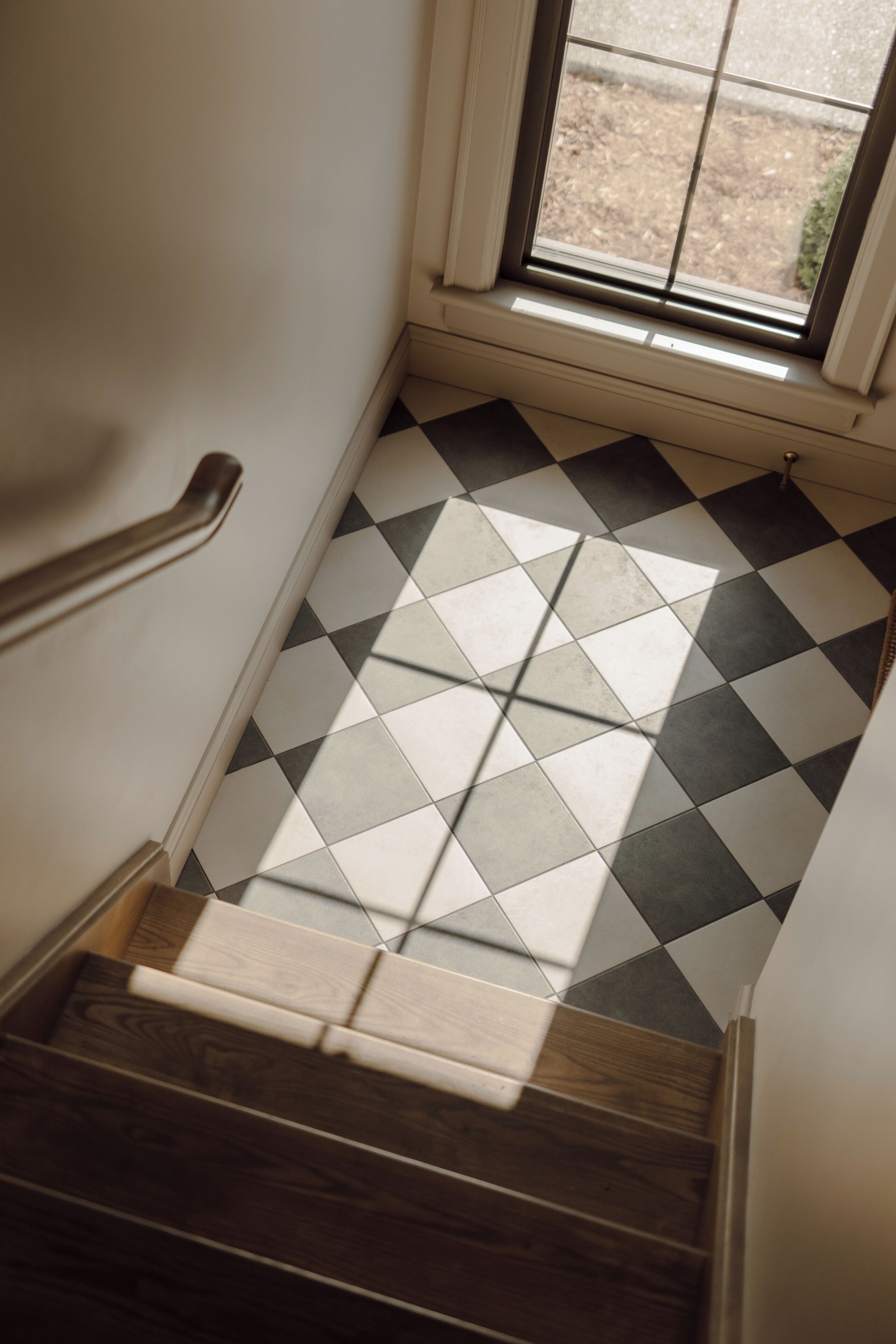 A staircase with a checkered tile floor, wooden steps, and a handrail.