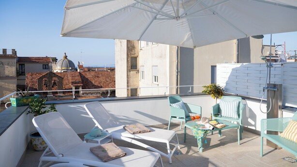 Une terrasse sur le toit avec des chaises longues blanches, une table agrémentée d’une plante et un grand parasol.