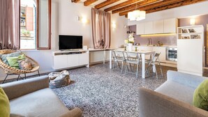 Ein modernes Wohnzimmer mit Fernseher, Sitzecke und einer Küche im Hintergrund.