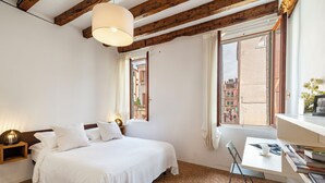Ein Schlafzimmer mit Bett, Nachttischen, Schreibtisch und einem Fenster mit Blick auf Gebäude.