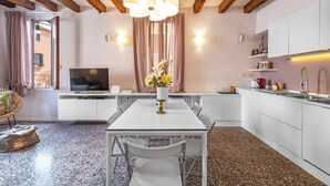 Eine moderne Küche mit weißen Schränken, einem Esstisch mit Stühlen, einem Fernseher und einer Blumenvase.
