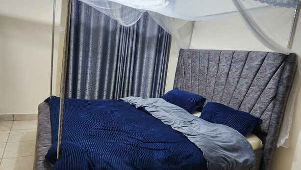 Un lit avec une tête de lit grise, une literie bleue et un ciel de lit blanc.