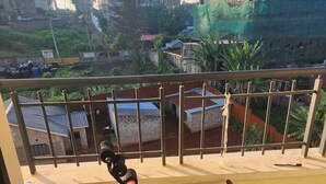 Un balcon équipé d’un vélo d’appartement, d’une paire de chaussons et offrant une vue sur un chantier de construction avec des bâtiments et des échafaudages.