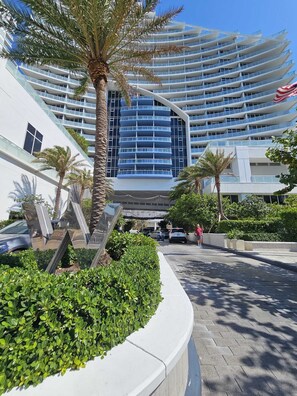 A modern hotel with a curved facade, multiple balconies, and a palm tree in the foreground. - Fort Lauderdale Beach Condo - We Host (Fort Lauderdale)