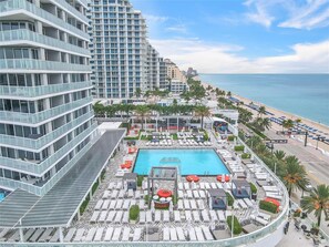 A rooftop pool area with lounge chairs and a swimming pool, surrounded by high-rise buildings and a beach. - Fort Lauderdale Beach Condo - We Host (Fort Lauderdale)