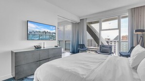 A modern hotel room with a large bed, a flat-screen TV mounted on the wall, a city view through large windows, a grey dresser, and a blue chair. - Lux Two BR Suite at W Fort Lauderdale (Fort Lauderdale)