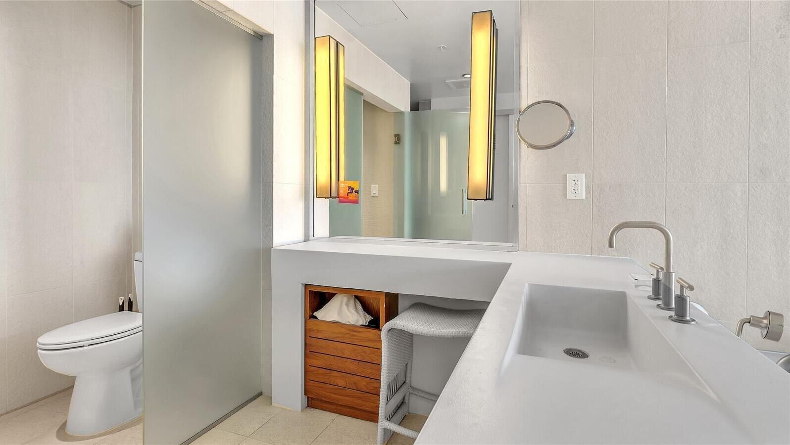 A modern bathroom with a white toilet, a large mirror, a white sink with a single faucet, and a towel rack.