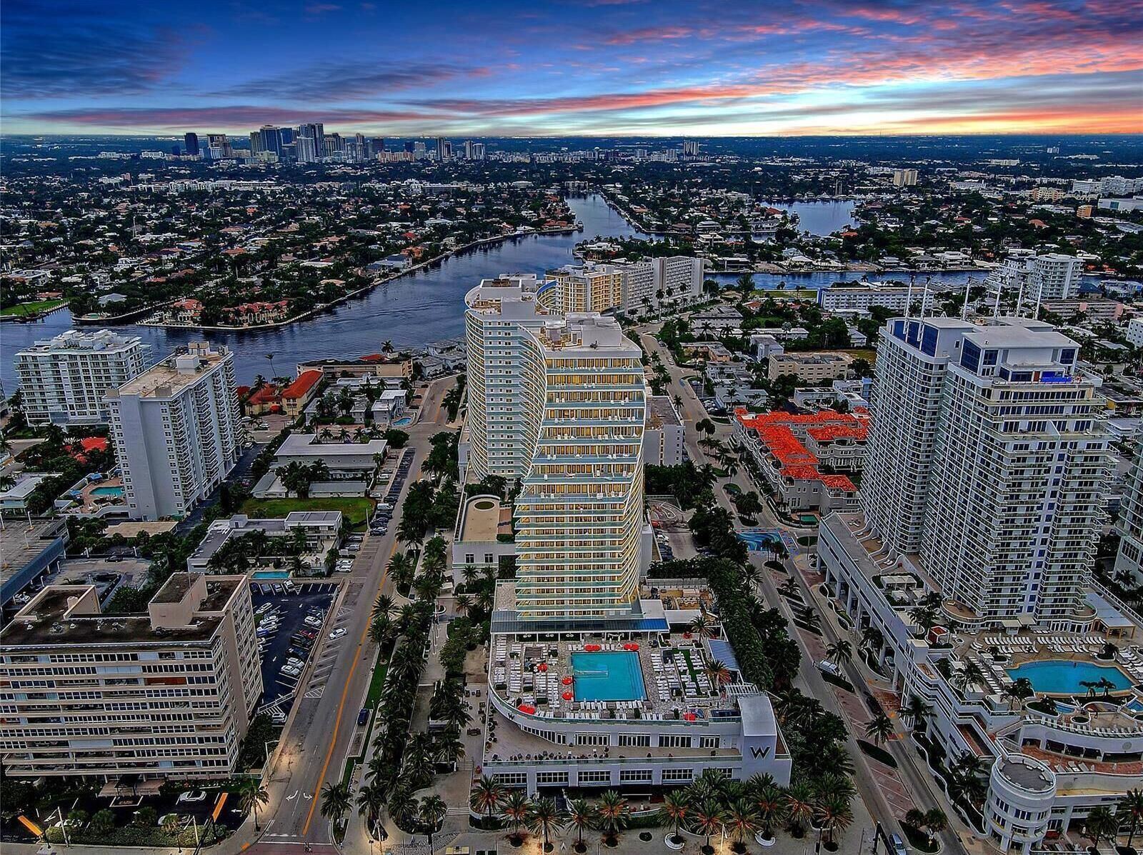 Un hotel moderno de gran altura con varias plantas, piscina y vistas a un río y al horizonte de la ciudad.