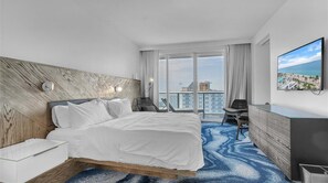 A hotel room with a large bed, a desk, a chair, a TV, and a view of the city. - Fort Lauderdale Beach Condo - We Host (Fort Lauderdale)