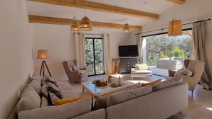 A spacious living room with a sofa set, a coffee table with decorative items, a television, and a balcony with outdoor furniture. - Villa Antassi  14 minute stroll to restaurants, wellness facilities, the beach (Grimaud)