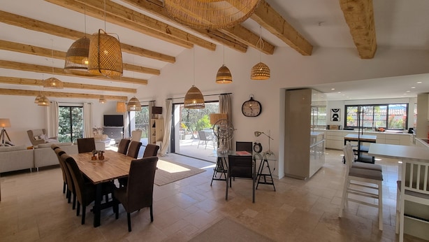 A spacious living area with a wooden dining table, comfortable seating, and a large window offering a view of the outdoors. - Villa Antassi  14 minute stroll to restaurants, wellness facilities, the beach (Grimaud)