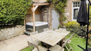 Ein Patio mit Holztisch und -stühlen, einem Whirlpool und einer Steinmauer.