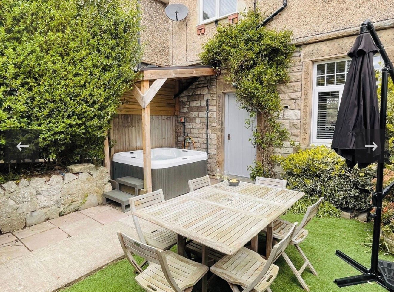 A patio with a wooden table and chairs, a hot tub, and a stone wall.