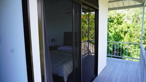 Enjoy a peaceful retreat with a balcony overlooking lush greenery, featuring a comfortable bed and a window with a metal screen.
