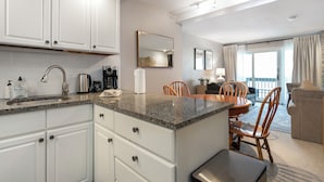 A modern kitchen with white cabinets, granite countertops, and a dining area with a wooden table and chairs. - Beautifully, Cozy Condo, Steps from Complimentary Shuttle, Free parking (Vail)